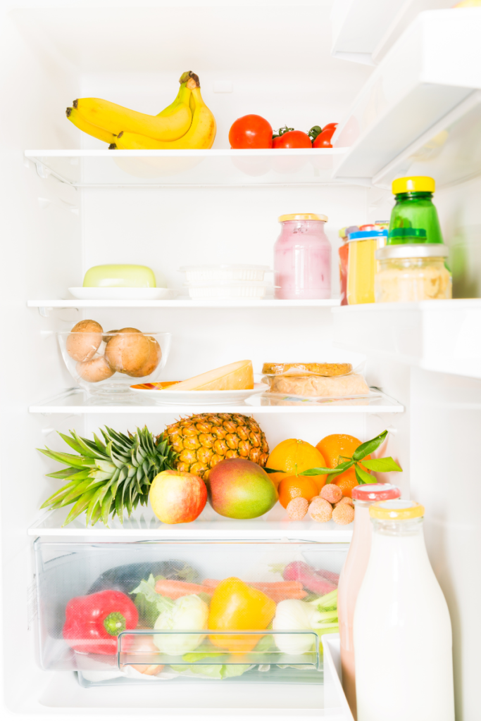 A clean, white fridge filled with various food items like fruits, veggies, and condiments