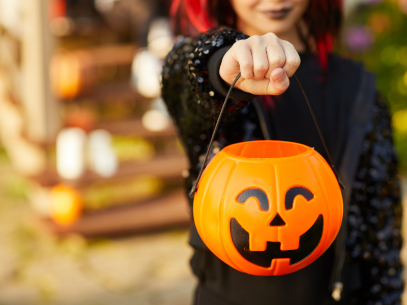 A trick or treater dressed up in a Halloween costume with a pumpkin candy basket