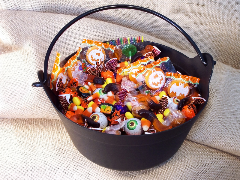 Leftover Halloween candy sitting in a black Halloween basket on beige fabric