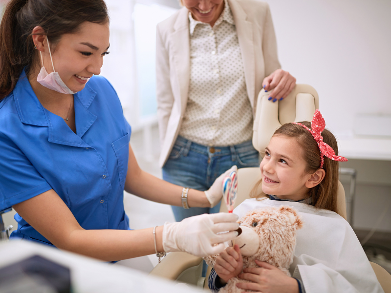 A dentist in blue scrubs handing treats to a young patient