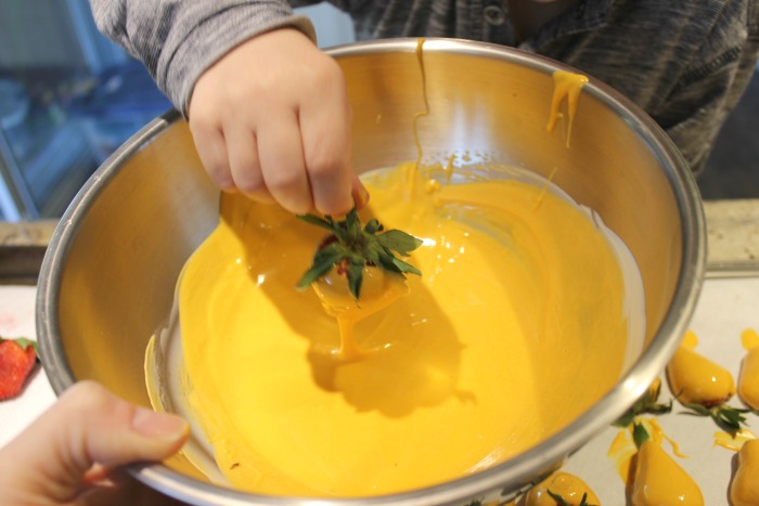 Dipping a strawberry into a bowl of melted white chocolate that has been tinted yellow