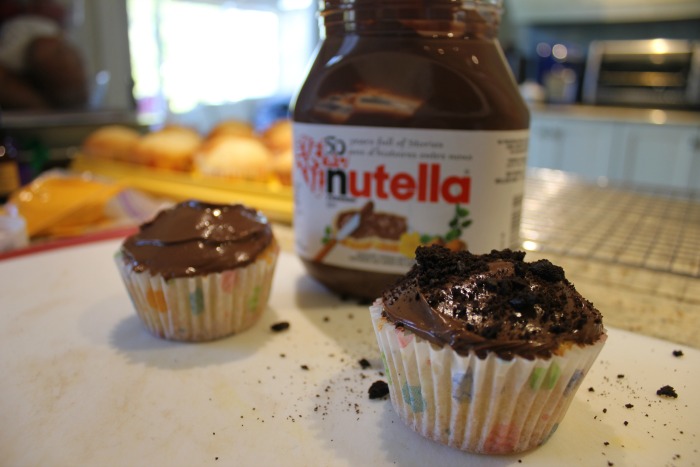 Two Nutella chocolate cupcakes, side by side, in front of a large jar of Nutella