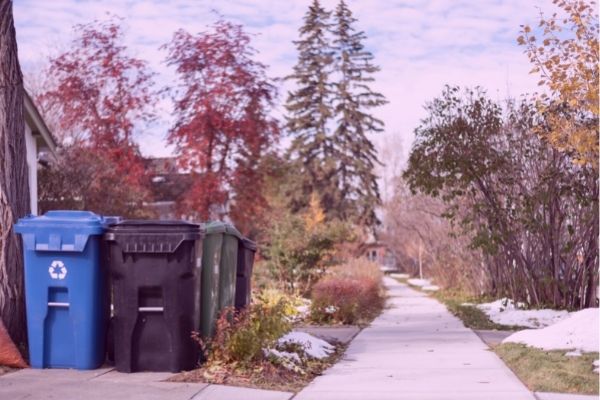 A view of a garbage and recycling pin with fall trees in the background