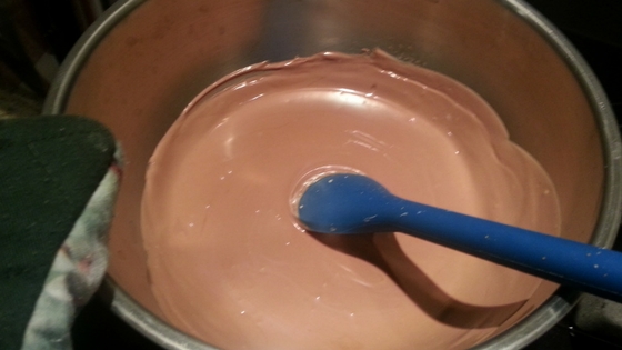 Melted chocolate in a sauce pan, being stirred with a blue spoon