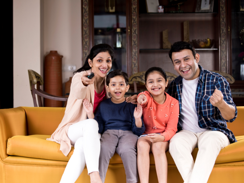 A family of four sitting on a yellow couch, watching television