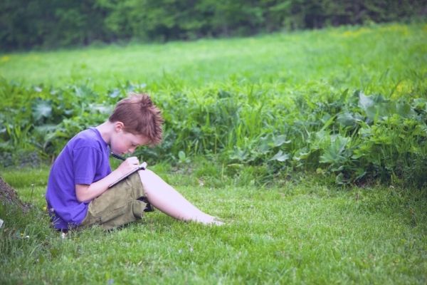 Young boy writing in journal in an open field